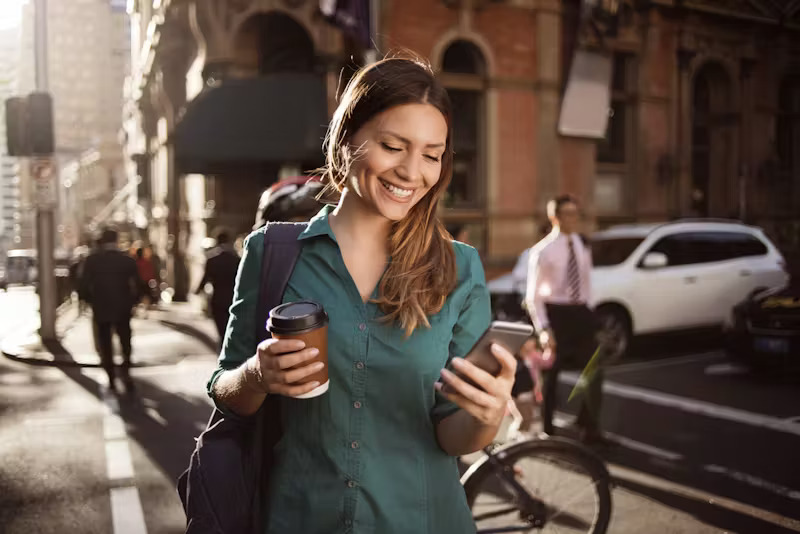 Woman holding coffee and phone, smiling with confidence and energy