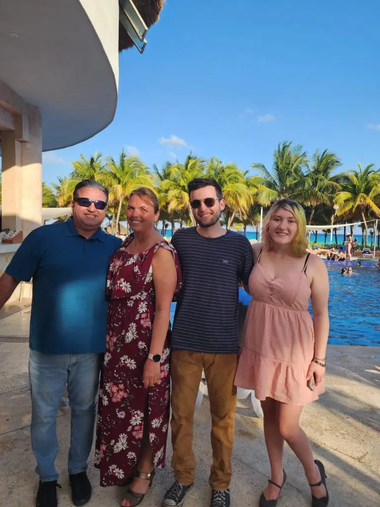 Group of four adults posing together by a resort pool with palm trees and blue sky behind them.